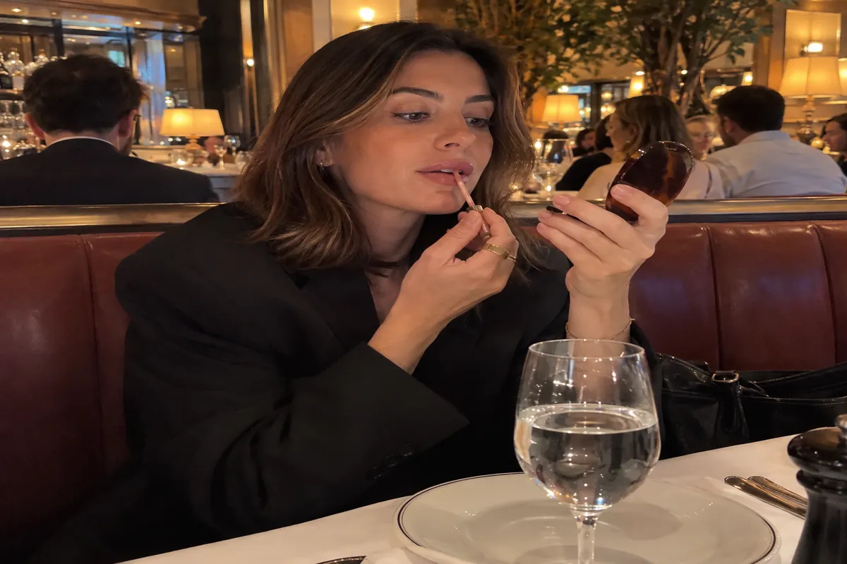 A woman in a restaurant booth touches up her lips before a business lunch, with a glass of water on the table